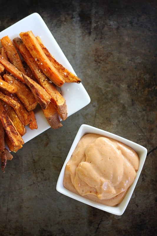 sweet potato fries on white tray with fry sauce in white square bowl.