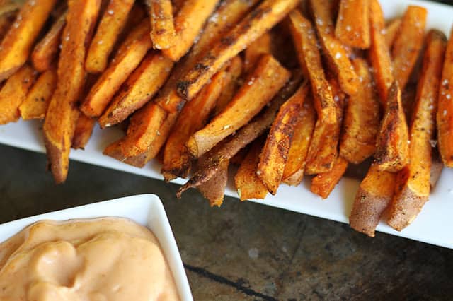 sweet potato fries on white tray with fry sauce in white square bowl.