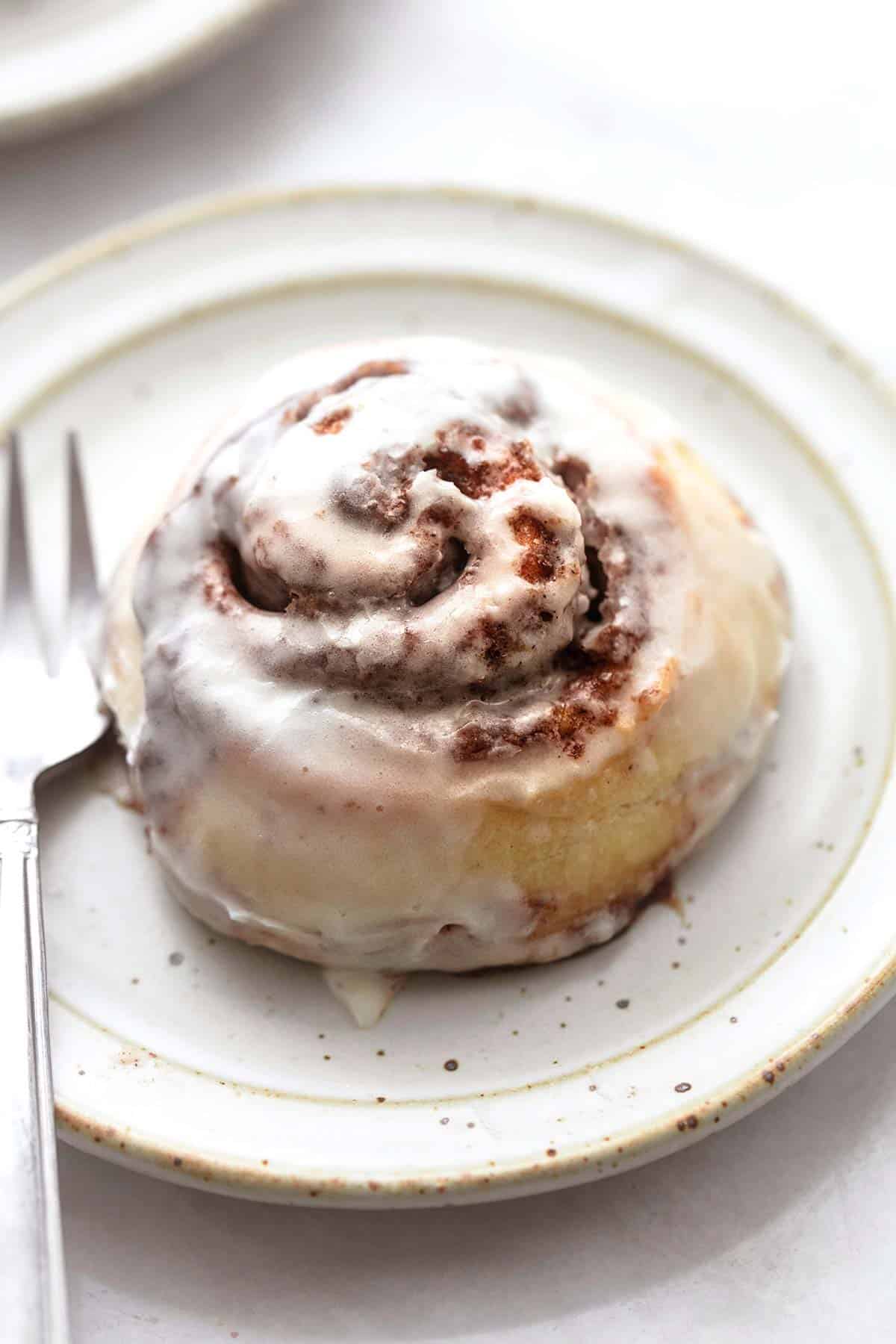 close up of a frosted cinnamon roll with a fork on a plate.