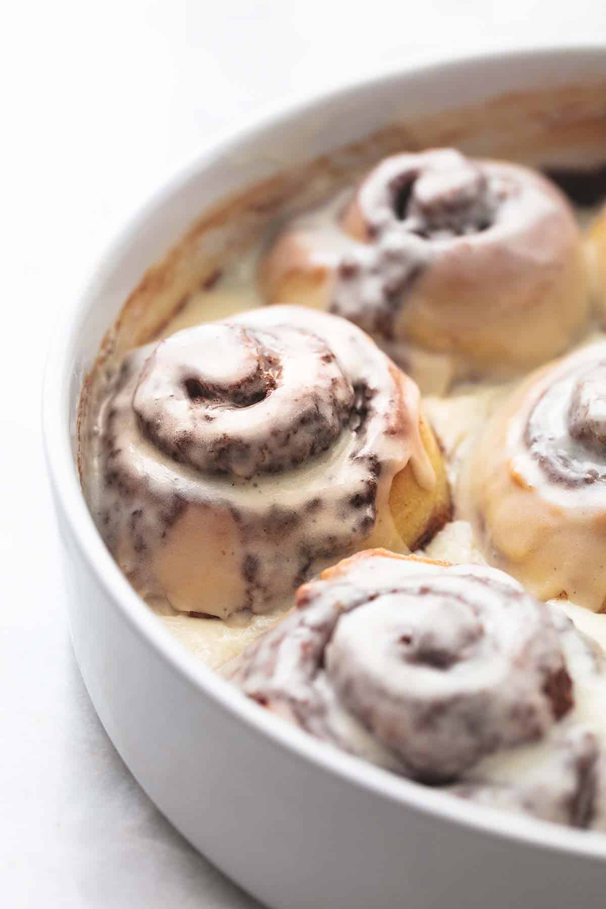 close up of frosted cinnamon rolls in a round white dish.