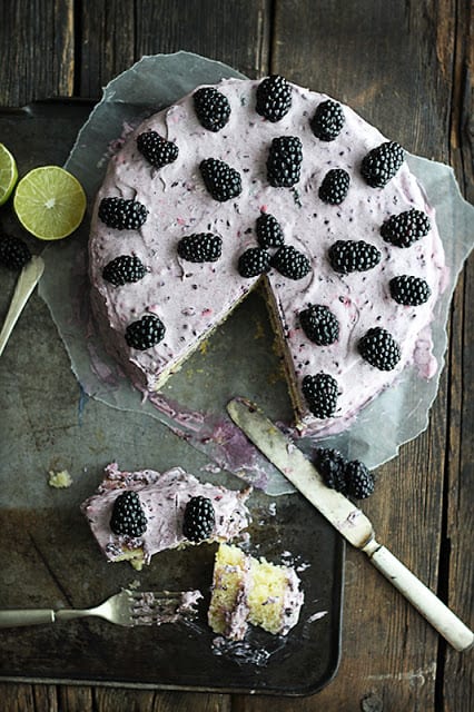 blackberry lime cake on baking sheet with a half eaten slice, limes, and a dirty fork and knife.