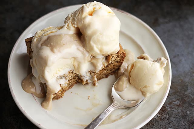 blondie sundaes with hot maple cream sauce on white plate with a spoon with a scoop on it.