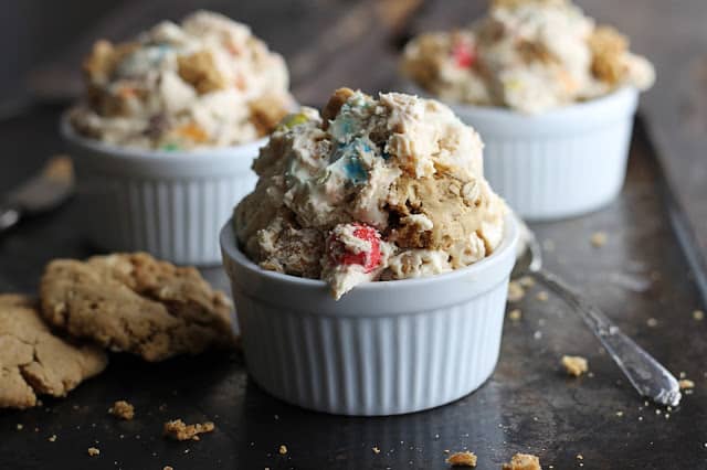 three small white bowls filled with ice cream on a baking sheet with a spoon and cookies.