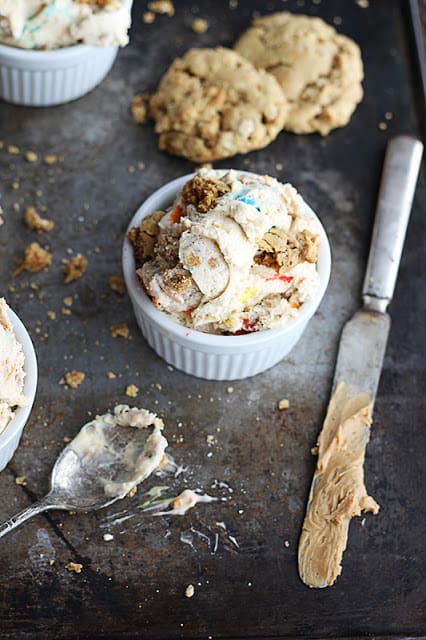 ice cream in a small white bowl on a baking sheet with a dirty spoon, knife and cookies.