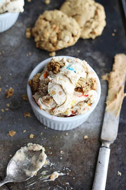 small white bowl with ice cream on a baking sheet with cookies, a dirty spoon and knife.