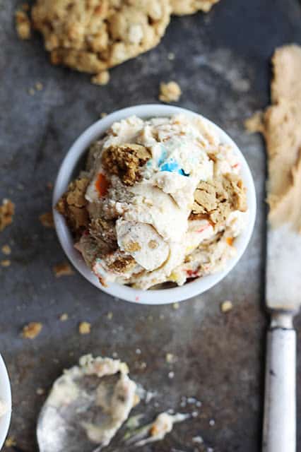 top view of a small white bowl filled with ice cream on a baking sheet with cookies, a dirty spoon and knife