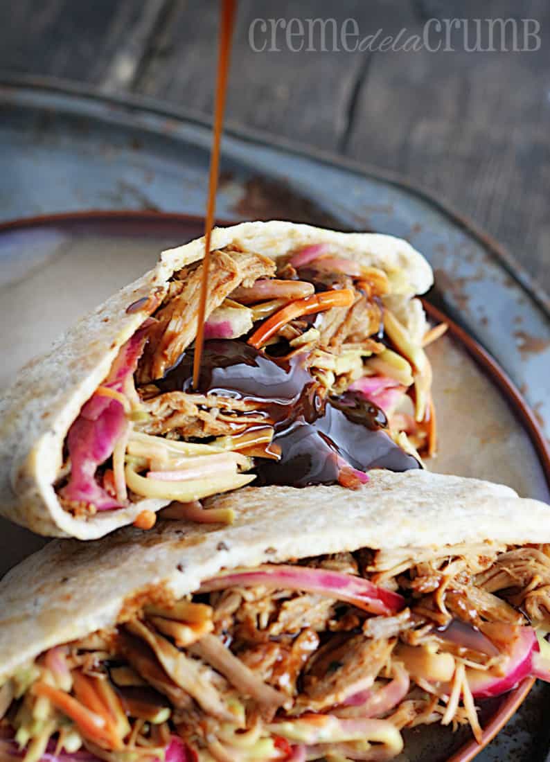 bbq pork pitas with slaw on a plate with bbq sauce being poured on them.