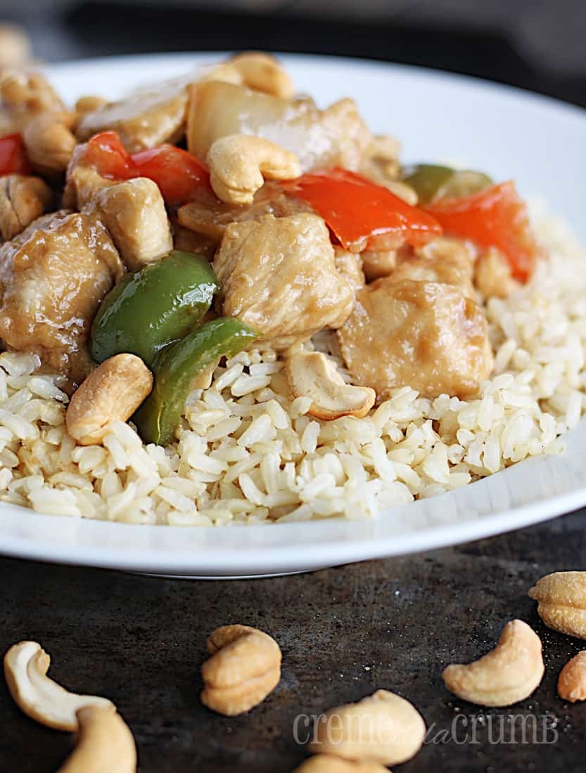 cashew chicken on rice in a white bowl on a baking sheet with cashews.