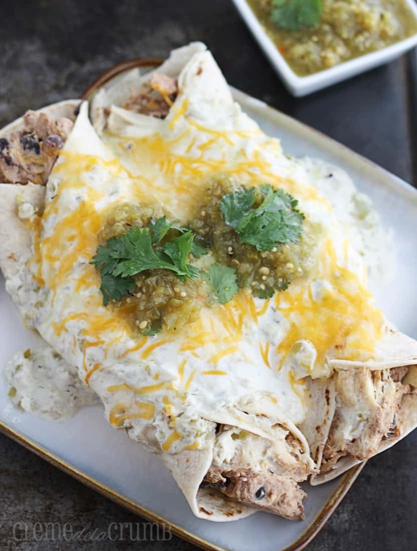 two enchiladas on a plate with salsa verde in white square bowl in the background.