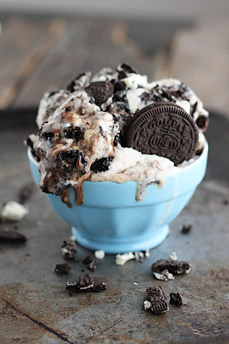 ice cream in small blue bowl on a baking sheet with crushed Oreos.