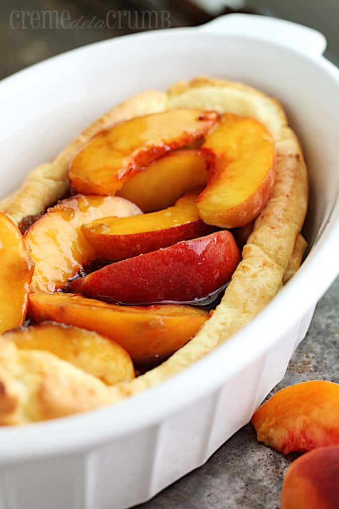 puff pancake topped with peaches in a round serving tray.
