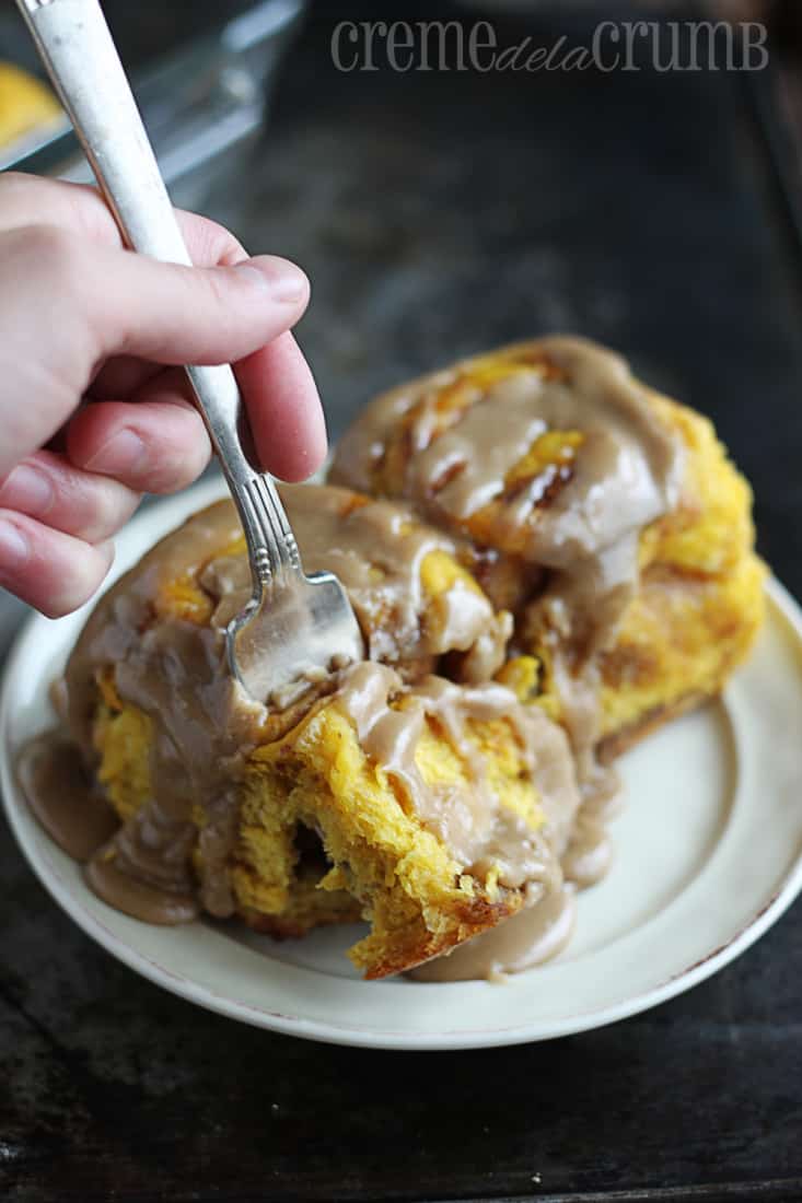 a hand taking bite with a fork out of the cinnamon rolls on a plate.
