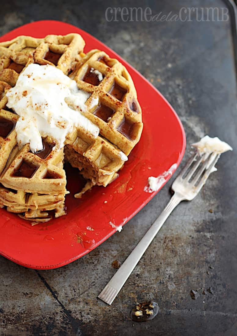 waffles on a red plate with a bite missing and a dirty fork on the side.
