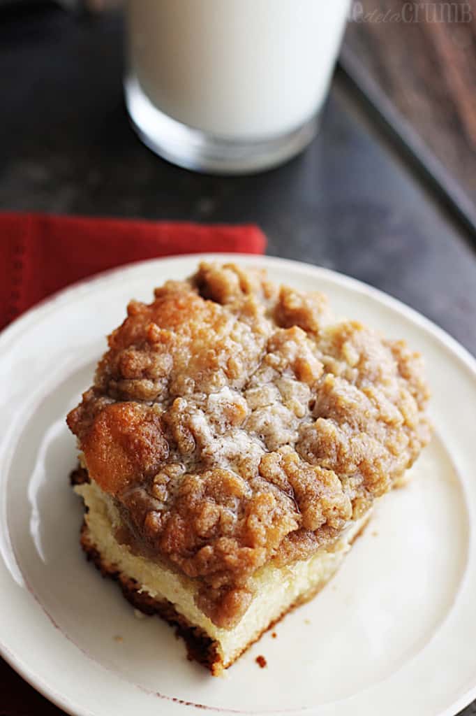 top view of a piece of crumb cake on a plate with a glass of milk.