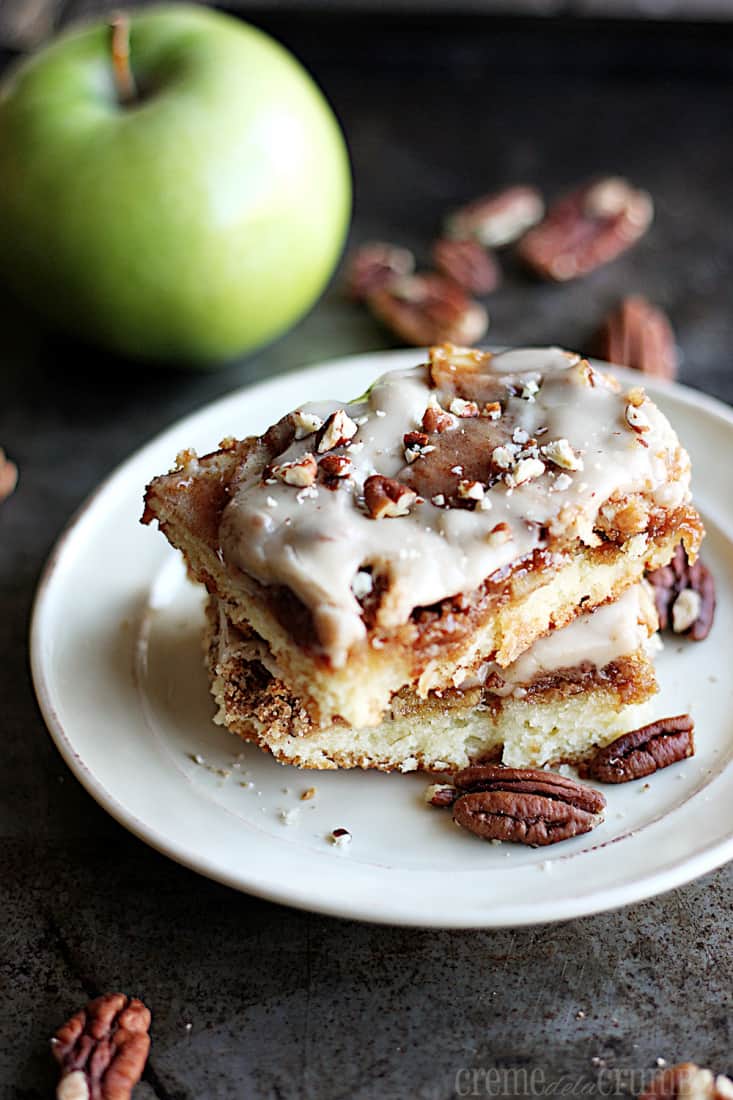 stacked maple pecan apple pie bars on a plate with pecans and a green apple faded in the background.