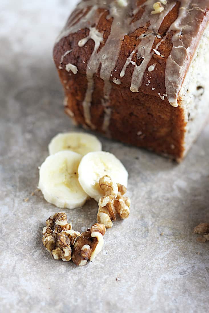 slices of banana and macadamia nuts next to a loaf of maple walnut banana bread.
