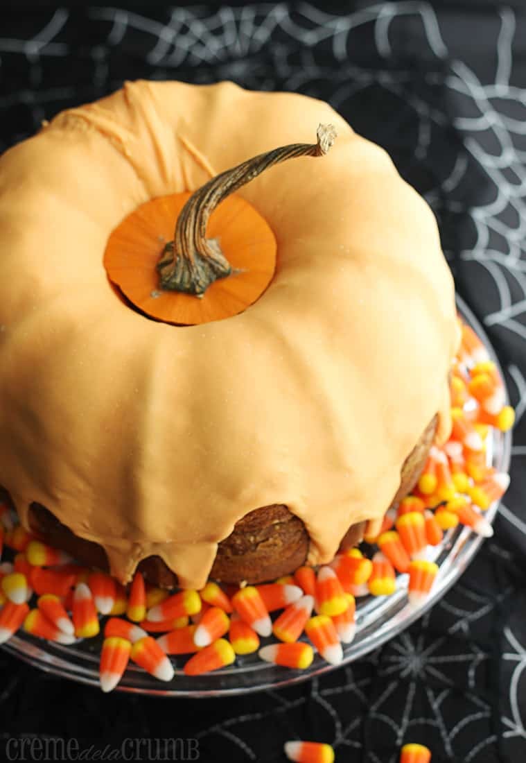 bundt cake on a cake platter with pumpkin stem on the top and candy corn on top of a spider web table cover.