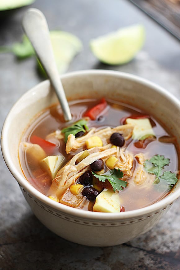 baja chicken soup in a bowl with a spoon and slices of a lime faded in the background.