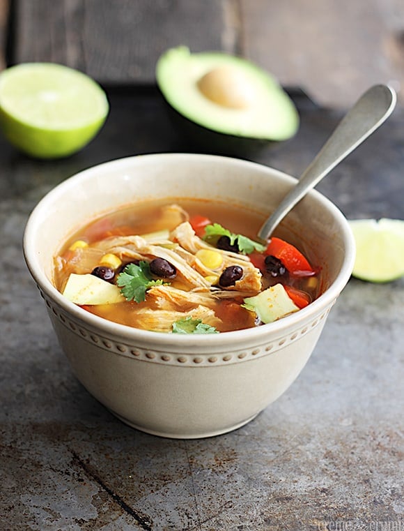 baja chicken soup in a bowl with a spoon and half a lime and half an avocado faded in the background.