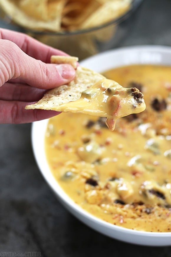 a hand holding a chip dipped in beef n' queso dip.