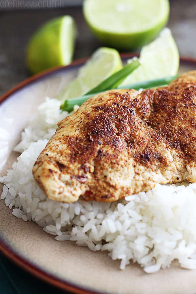 cajun chicken on rice with green onion and slices of a lime on a plate with a slice and a half of a lime faded in the background.