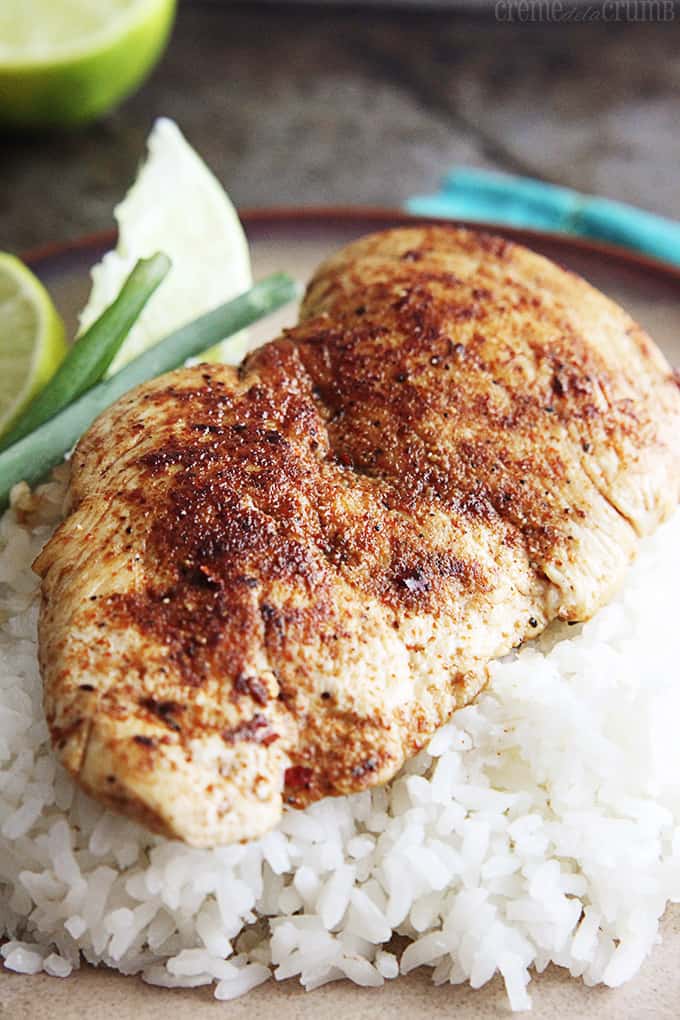 cajun chicken on rice with green onions and slices of a lime on a plate.