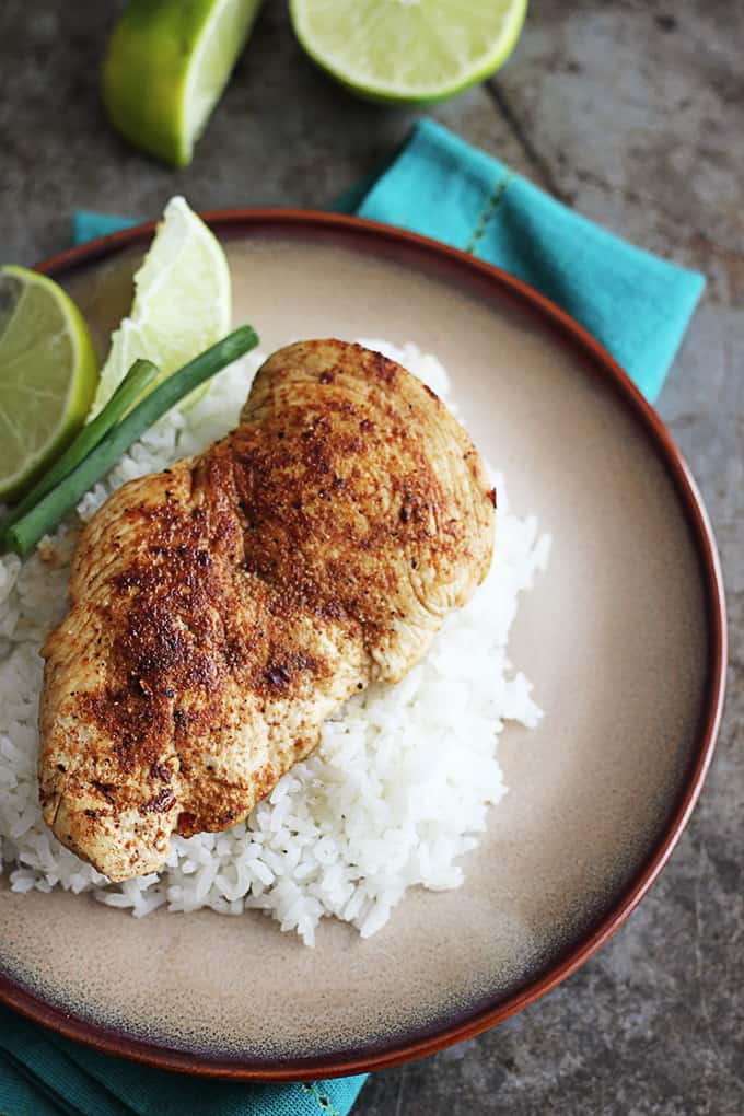 top view of cajun chicken on rice with green onions and slices of lime on plate on a blue cloth napkin.