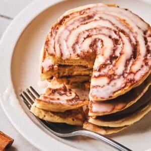 Cinnamon roll pancakes with a fork on a plate with a bite out of the pancakes on the fork.
