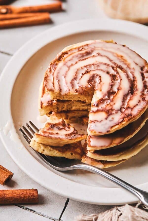 Cinnamon roll pancakes with a fork on a plate with a bite out of the pancakes on the fork.