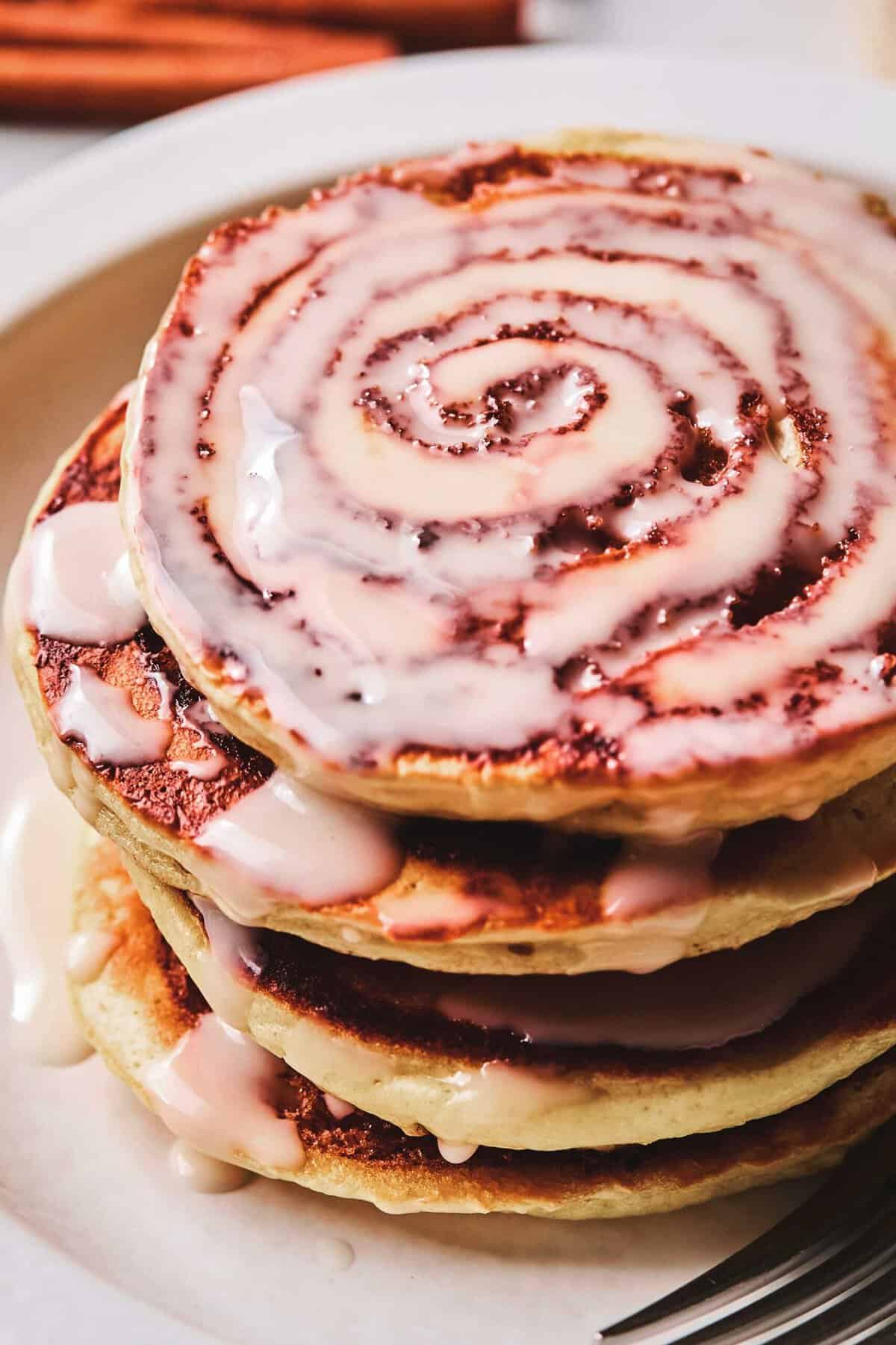 Close up of a stack of cinnamon roll pancakes on a plate.