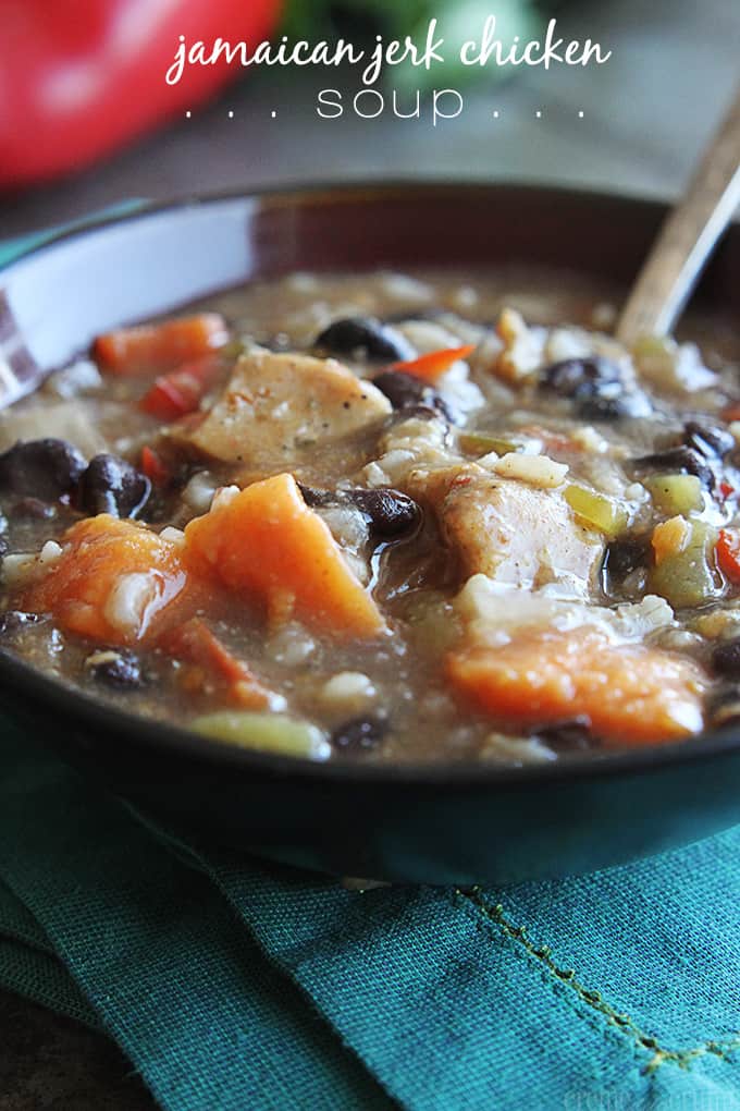 Jamaican jerk chicken soup in a bowl with a spoon on a blue cloth napkin with the title of the recipe written on the top of the image.