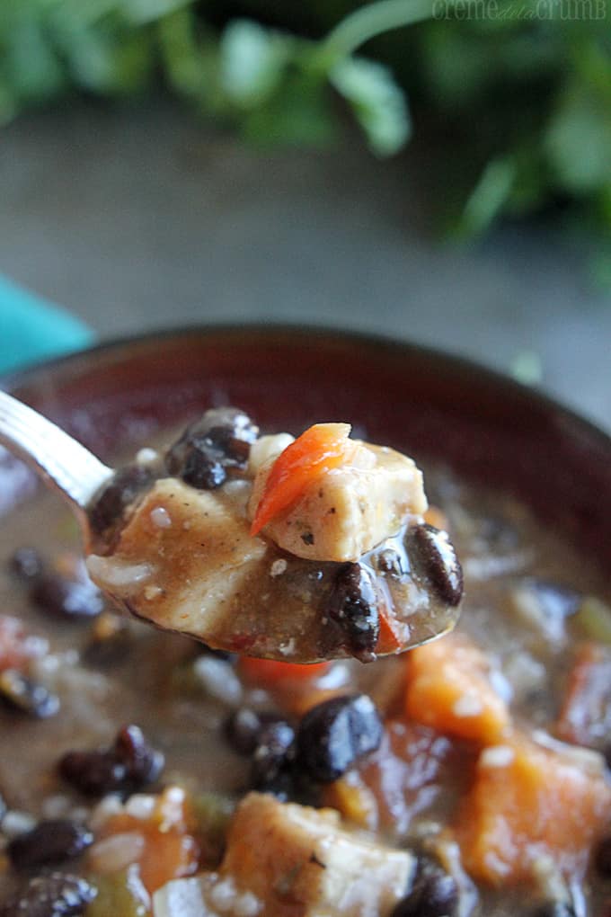 a spoon lifting a bite of Jamaican jerk chicken soup from a bowl.