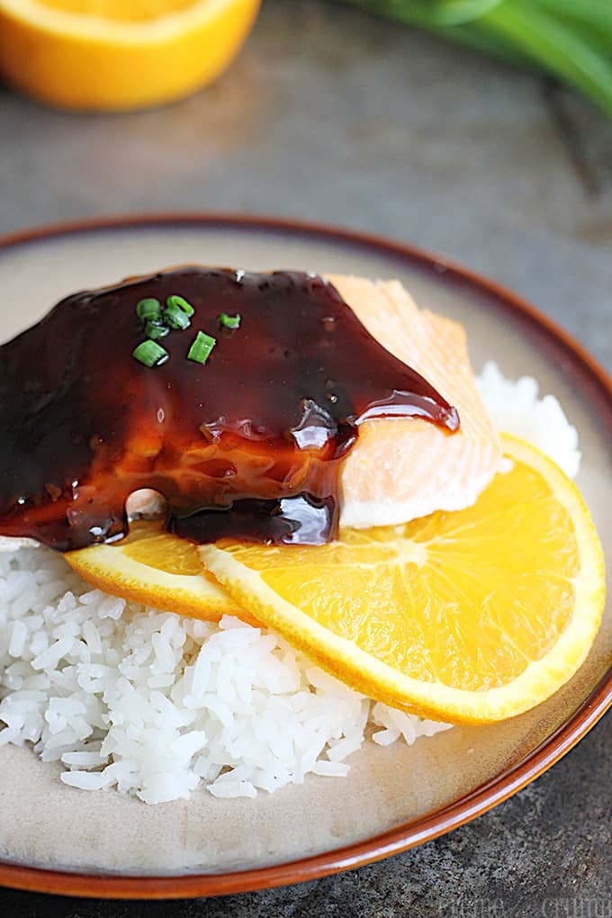 orange teriyaki salmon on orange slices on rice on a plate.