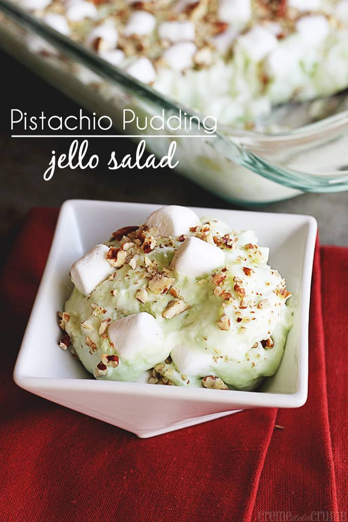 pistachio pudding jello salad in a small square bowl on a red cloth napkin with a baking tray filled with pistachio pudding jello salad faded in the background with the title of the recipe on the top left side of the image.