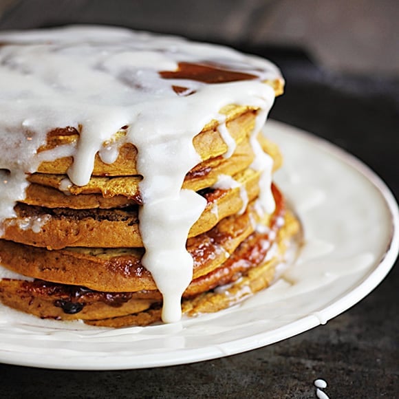 pumpkin cinnamon roll pancakes covered with cream cheese vanilla glaze on a plate.