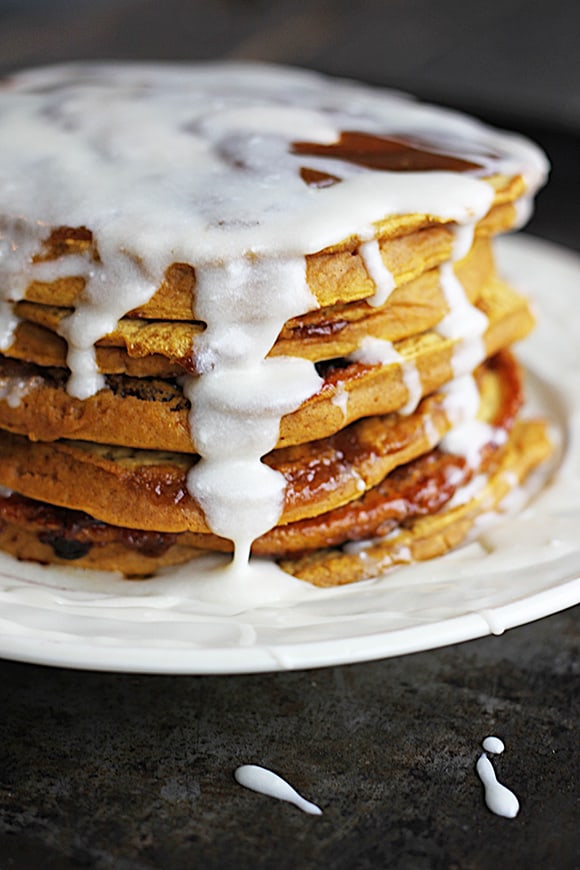 pumpkin cinnamon roll pancakes with cream cheese vanilla glaze on a plate.