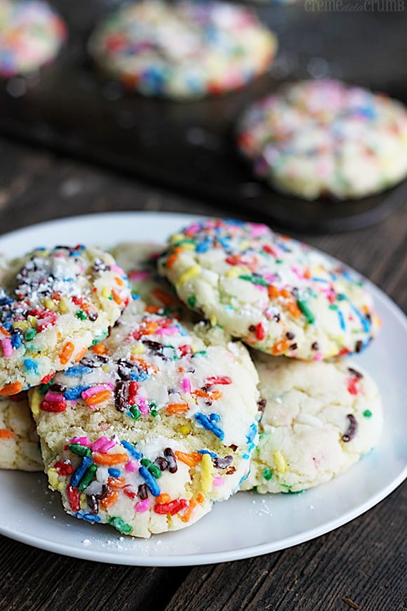 sprinkle crinkle cookies on a plate with more sprinkle crinkle cookies on a baking sheet faded in the background.