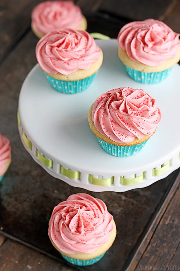 sugar cookie cupcakes on a cake platter on a baking sheet with more sugar cookie cupcakes.