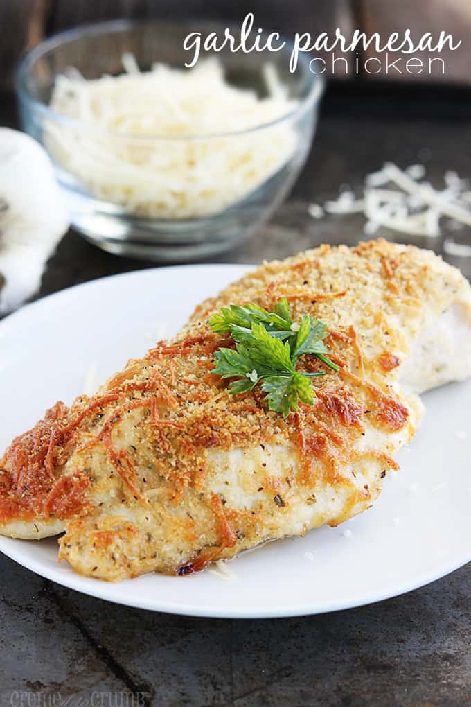 garlic parmesan chicken on a plate with parmesan cheese in a bowl faded in the background with the title of the recipe written on the top right corner of the image.