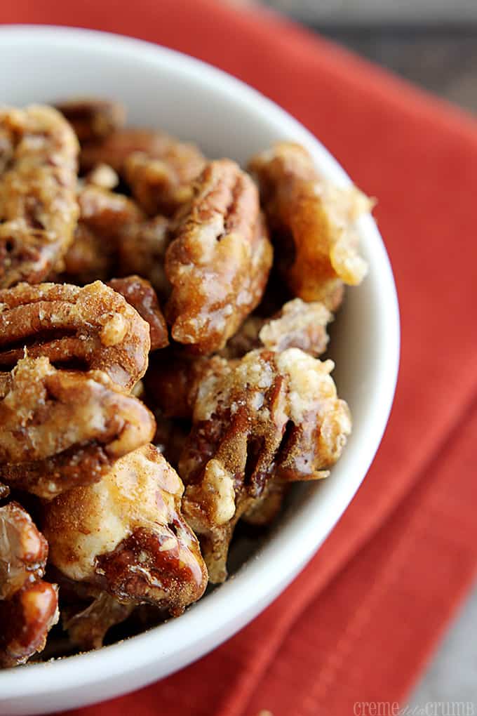 close up of candied cinnamon pecans in a white bowl on top of a red cloth napkin.