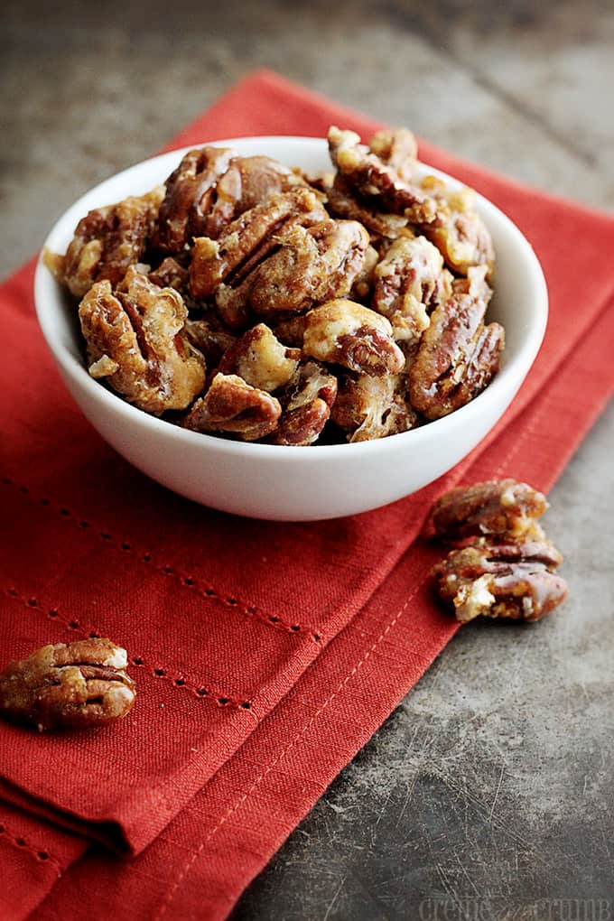 candied cinnamon pecans in a white bowl on top of a red cloth napkin with pecans on the side.