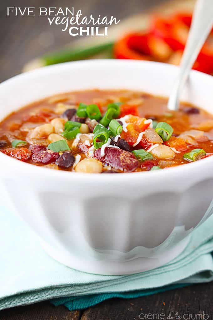 five bean vegetarian Chili with a spoon in a bowl on a green cloth napkin with the title of the recipe written on the top left corner of the image.