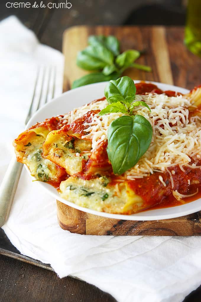 cheesy meatless manicotti  on a wooden cutting board on a white cloth napkin with a fork on the side.