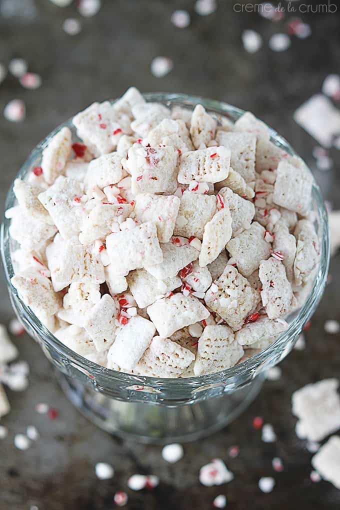 top view of peppermint crunch muddy buddies in a glass pedestal bowl on a baking sheet with more peppermint and muddy buddies on top.