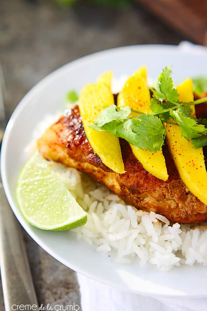 sweet paprika chicken on rice topped with mango slices and cilantro leaves with slices of a lime on the side of the plate.
