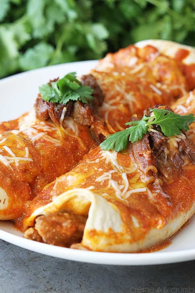 sweet pork enchiladas on a plate with a bundle of cilantro faded in the background.