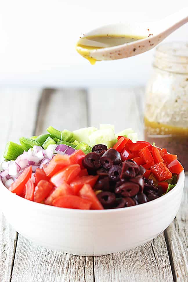 Greek chopped salad in a bowl with a spoon pouring Greek dressing on top.