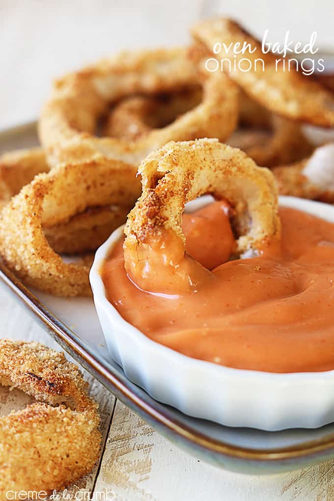 oven baked onion rings on a tray with sauce and an onion ring dipped in the sauce with the title of the recipe written on the top right corner of the image.