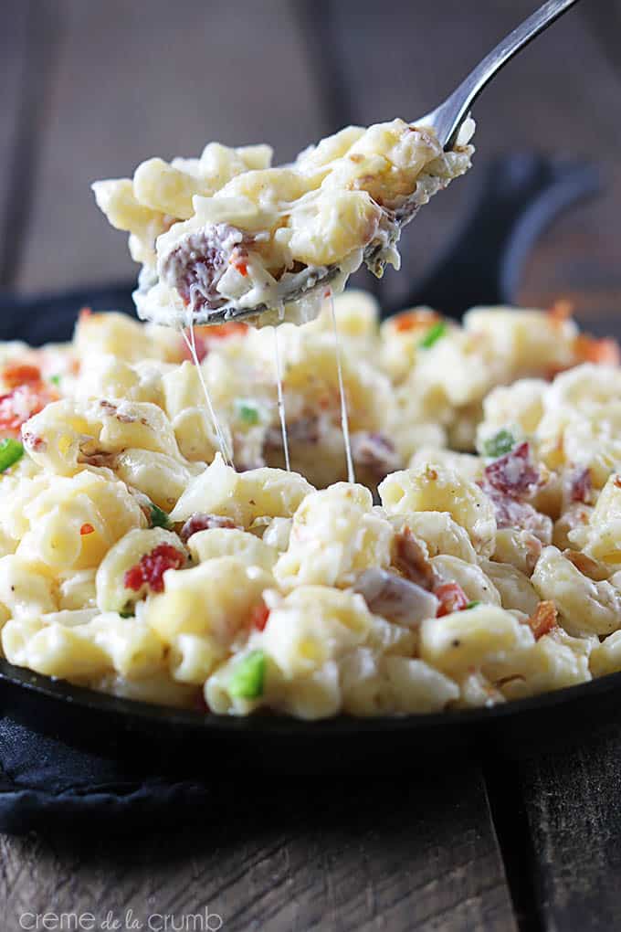 a spoon lifting a bite of pepper-jack bacon mac n' cheese from a skillet.