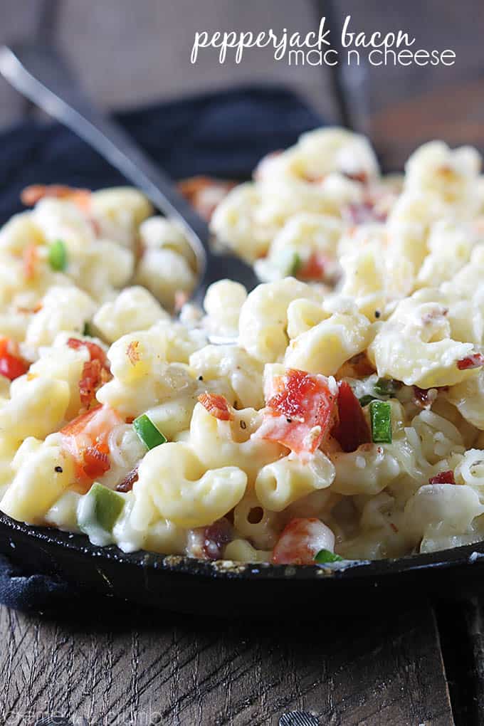 pepper-jack bacon mac n' cheese with a spoon in a skillet with the title of the recipe written on the top right corner of the image.
